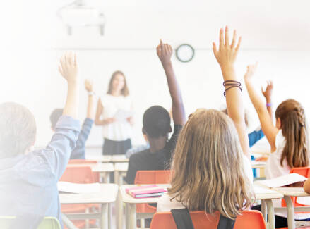 Back of the classroom view with students raising their hands
